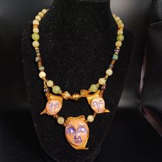 This is such an unusual handmade Artisian necklace made of beautiful glass beads and assorted stones with a second layer of the same beads and stones with porcelain painted moonman faces attached to a cut leather piece that hangs below the main beaded necklace. This fabulous necklace was created by a craftsman who was very passionate about their designs.  All types of Artisian works are time consuming and these skilled artists always pay close attention to every detail as each creation usually tells a story. This piece is signed Klein 08 or 98 on the reverse side of the larger center pendant as shown in photo.  There are a total of three moonman porcelain type faces that are painted with an irridescent purple paint on their eyes that highlights their faces.   This necklace measures approxi Adjustable Hand Painted Spiritual Necklaces, Unique Handmade Jade Necklaces, Unique Handmade Jade Necklace, Unique Collectible Round Beads Jewelry, Handmade Spiritual Czech Glass Crystal Necklace, Hand Painted Spiritual Jewelry For Festivals, Spiritual Hand Painted Jewelry For Festivals, Hand Painted Spiritual Round Necklaces, Unique Gemstone Beads