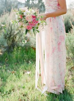 a woman holding a bouquet of flowers in her hand and wearing a long pink dress