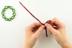 two hands are making beaded bracelets with red and green beads on white surface