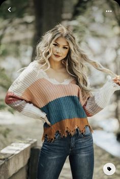 a beautiful woman posing for the camera in jeans and a colorful sweater with fringes