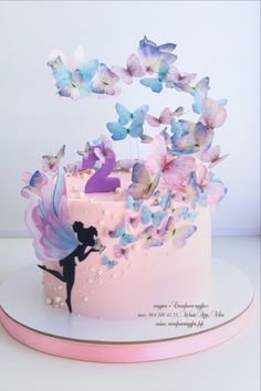 a pink cake decorated with butterflies and a fairy on the top is holding a candle