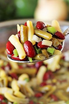 a spoon full of food that is on top of a bowl with noodles and beans