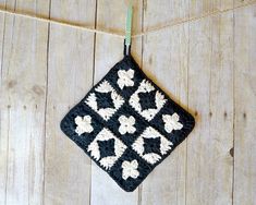 a black and white crocheted square hanging from a string on a wooden floor