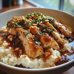 a white bowl filled with rice and meat covered in sauce on top of a wooden table