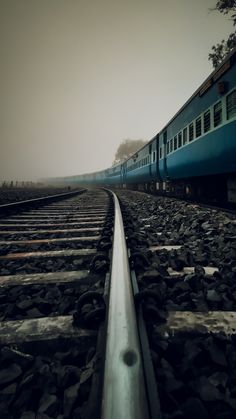 a blue train traveling down train tracks next to a forest on a foggy day