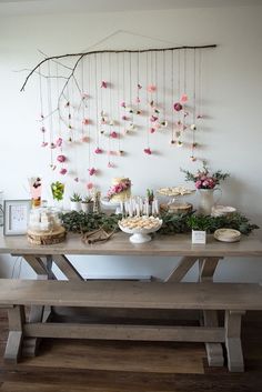 a table topped with lots of desserts and flowers next to a wall hanging from the ceiling