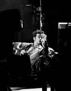 a black and white photo of a man sitting in a chair talking on the phone