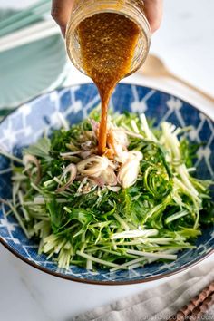 someone pouring dressing into a blue bowl filled with greens