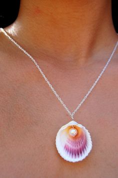 a woman wearing a necklace with a pink and orange shell on it's back