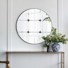 a round mirror sitting on top of a wooden shelf next to a vase with flowers