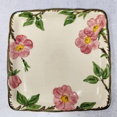 a pink flowered plate with green leaves and flowers on the edge is sitting on a white surface