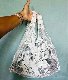 a hand holding a white net bag on top of a blue wall