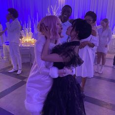 two girls in wedding dresses hugging each other at a party with purple lighting behind them