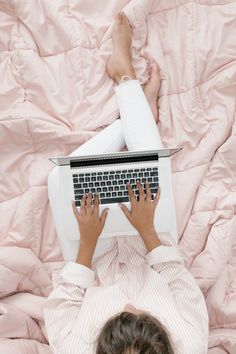 a woman laying in bed with her feet on the keyboard of an open laptop computer