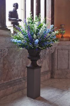 a vase filled with blue and white flowers sitting on top of a marble floor next to a statue