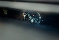 the reflection of a man in a car's steering wheel is seen through a window