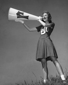 a woman in a dress holding a large white and black object while standing on top of a grass covered hill