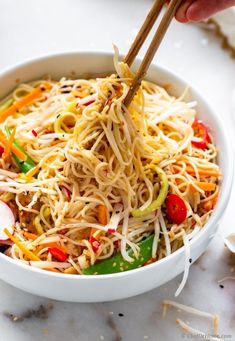 someone holding chopsticks over a bowl filled with noodles and vegtables