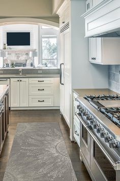 a large kitchen with white cabinets and stainless steel stove top oven next to an area rug