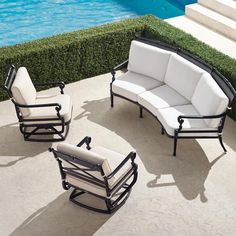 an outdoor patio furniture set with white cushions next to a swimming pool and green grass