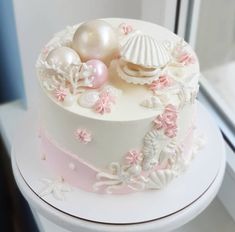 a white and pink cake with seashells on it's side sitting in front of a window