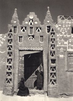 an old black and white photo of two people in front of a building with decorations on it