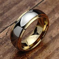 a gold and black wedding ring on top of a wooden table with the word love written in