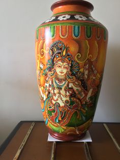 a colorful vase sitting on top of a wooden table next to a white wall in the background