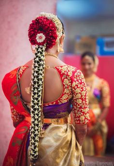 the back of a woman's head wearing a red and gold saree with flowers in her hair