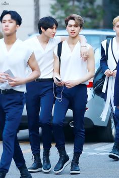 three young men in white shirts and blue pants are walking down the street with headphones on