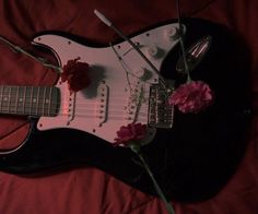 an electric guitar with flowers on it laying on a bed