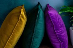 three different colored pillows sitting on top of a wooden table next to a potted plant