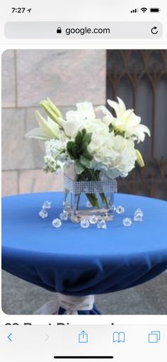 a blue table topped with a vase filled with white flowers and diamond brooches