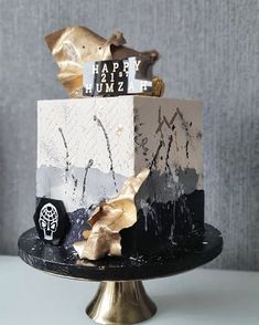 a black and white cake with gold foil decorations on it's top, sitting on a table