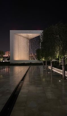 a large building with trees in front of it at night, and lights shining on the walls