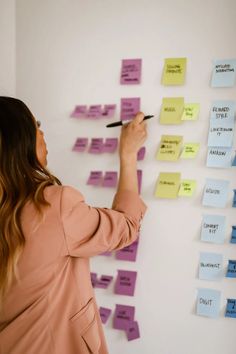 a woman writing on a wall with sticky notes