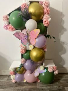 a number one made out of balloons with flowers and butterflies on it, sitting in front of a white wall