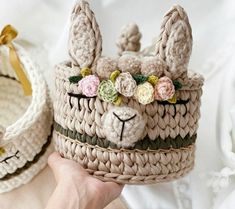 a person holding up a crocheted llama basket with flowers on it's head