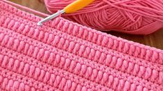 a pink crochet bag with a yellow handled knitting needle next to it and balls of yarn in the background