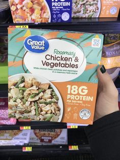 a person holding up a box of frozen chicken and veggies in a grocery store