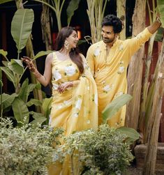 a man and woman dressed in yellow standing next to each other with palm trees behind them