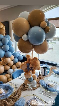 a teddy bear sitting on top of a table next to blue and gold balloons in the shape of trees