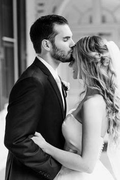 a bride and groom kissing in front of a building on their wedding day, black and white photo