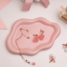 a pink tray with two heart shaped earrings on it next to flowers and other accessories