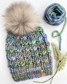 a knitted hat with a pom - pom on top and yarn next to it