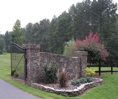 a stone wall and gate in the middle of a grassy area