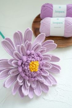 a purple crochet flower sitting on top of a wooden plate next to two balls of yarn