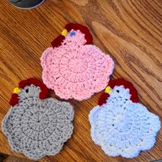 three crocheted rooster coasters sitting on top of a wooden table