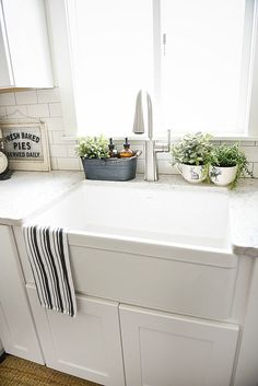 a white kitchen sink sitting on top of a counter next to a potted plant