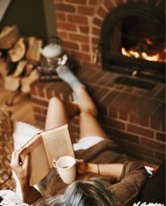 a woman laying on the floor reading a book and holding a coffee cup in her hand